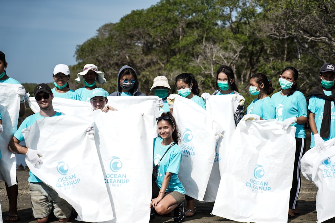 people in white shirt standing on green grass field during daytime community service group volunteering teenagers cleanup activity