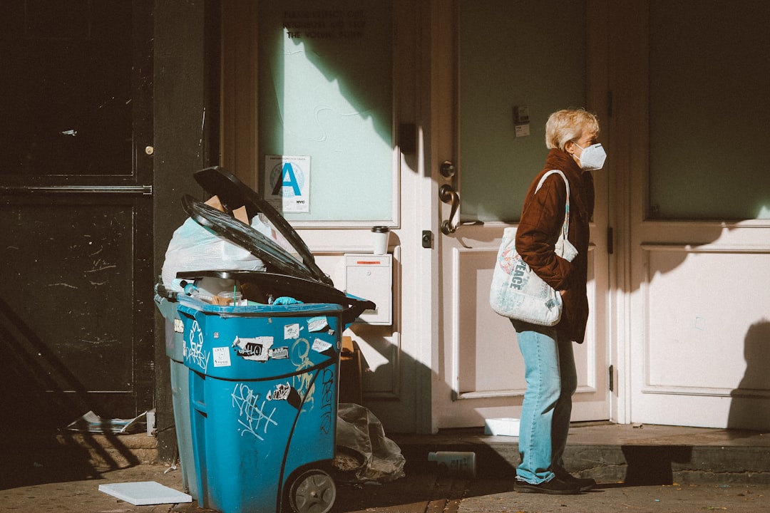 woman in brown jacket and blue denim jeans standing beside red plastic trash bin cleaning cart janitor waste bins