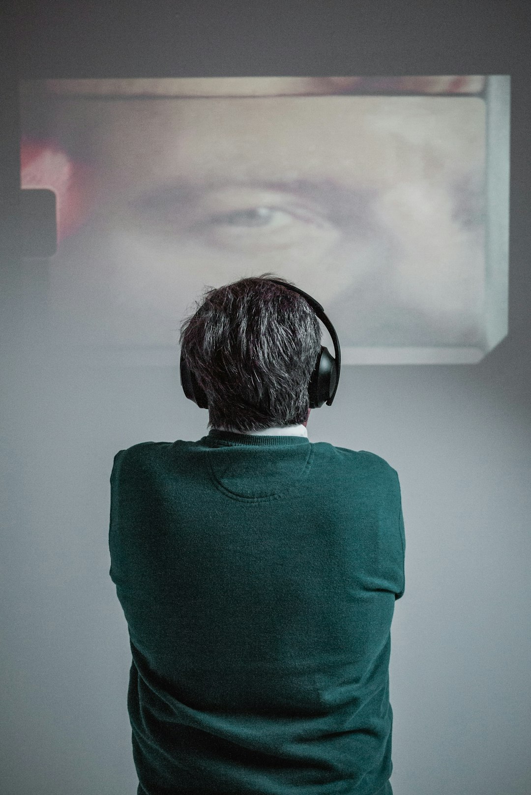 person wearing green shirt using black headphones while standing and facing back and watching movie voice clone multilingual video international audience