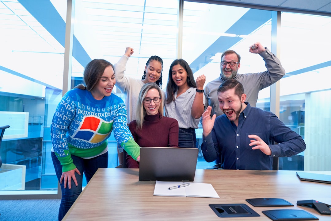 men and women sitting and standing by the table looking happy while staring at laptop diverse team happy employees workplace spotlight 2