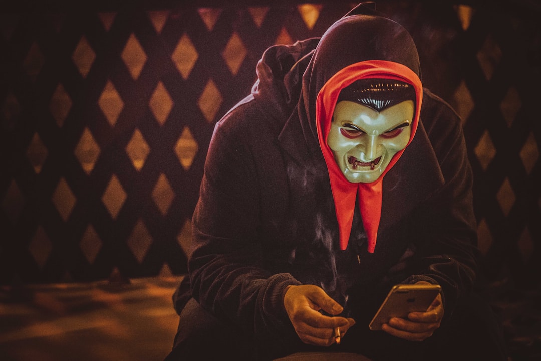 person in black and red mask holding smartphone scam alert fake tech support smartphone security
