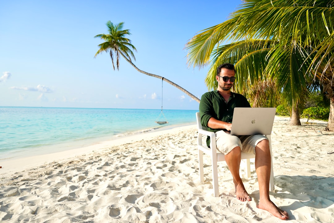 a man sitting in a chair on a beach using a laptop wordpress plugin dashboard vacation rental booking calendar integration