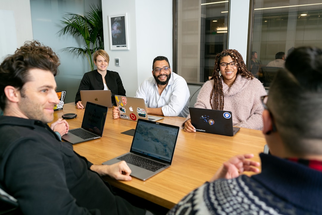 four people all on laptops two men and two women listen to person talking in a board meeting team meeting mentor apprentice modern workspace